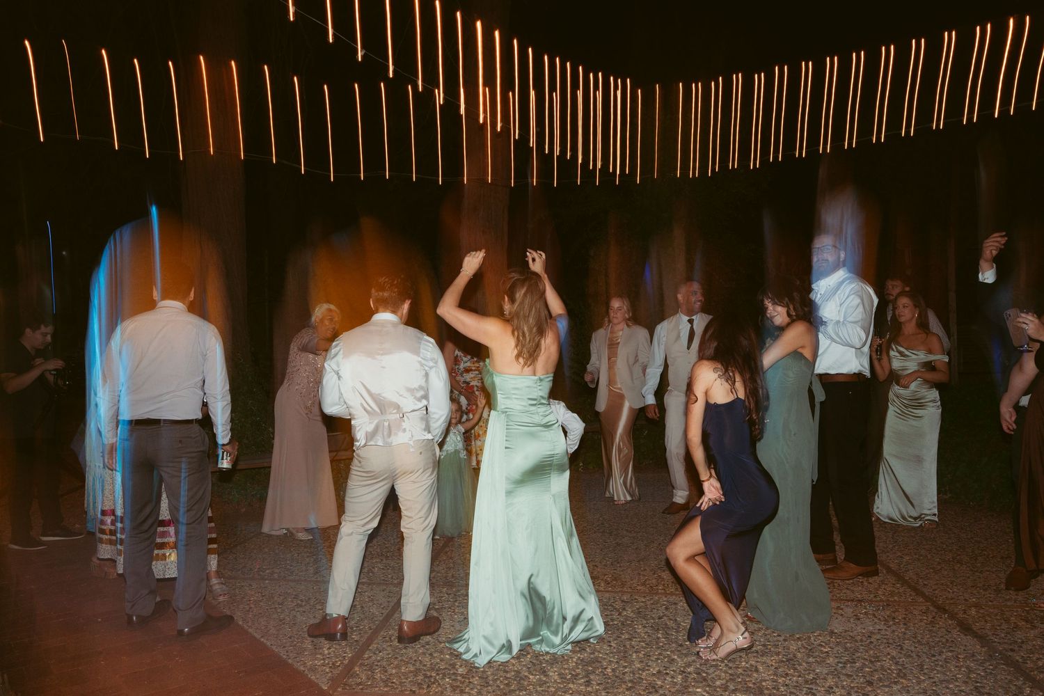 Wedding guests dancing on an outdoor patio under string lights at dusk.