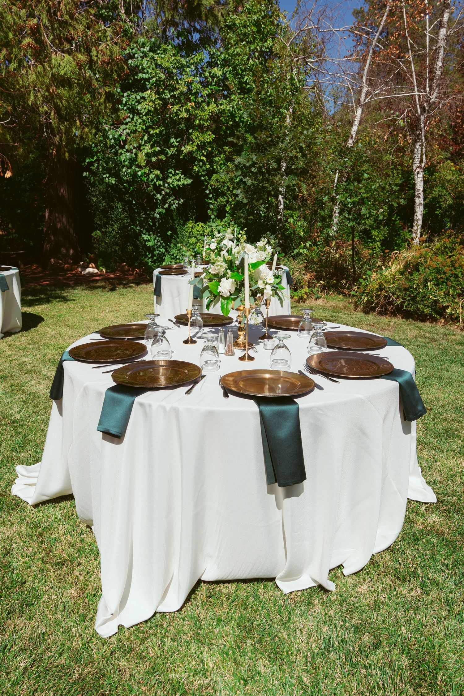 Elegant outdoor wedding table setting with white linens and dark napkins in a garden.