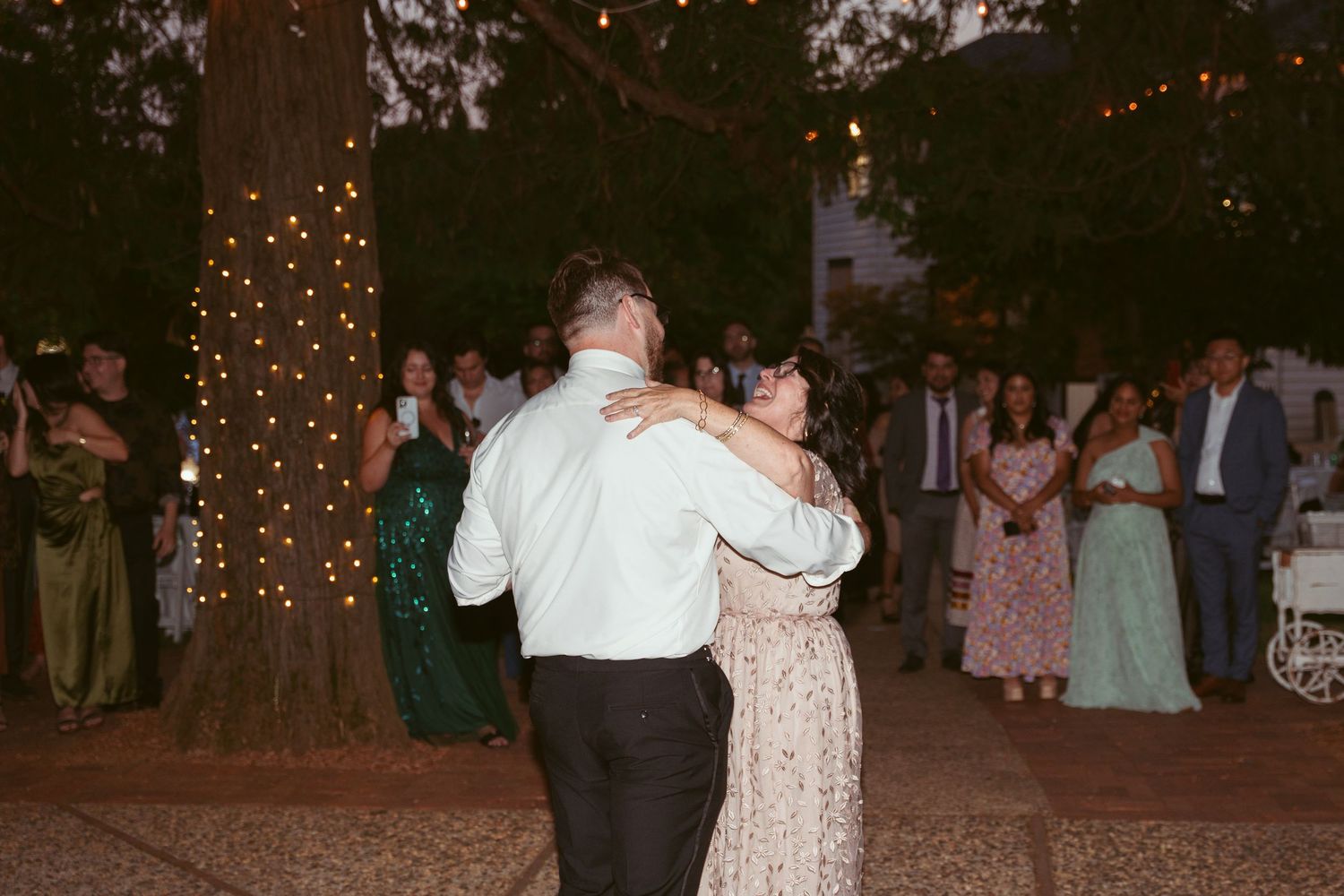 Couples share dances under twinkling lights at an evening outdoor wedding celebration.