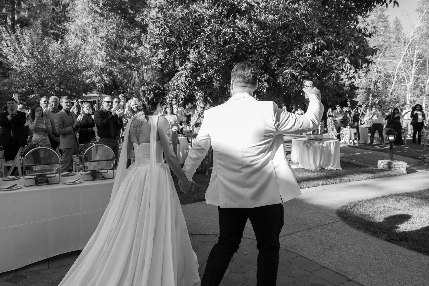 Black and white photo of couple greeting guests during outdoor wedding reception.