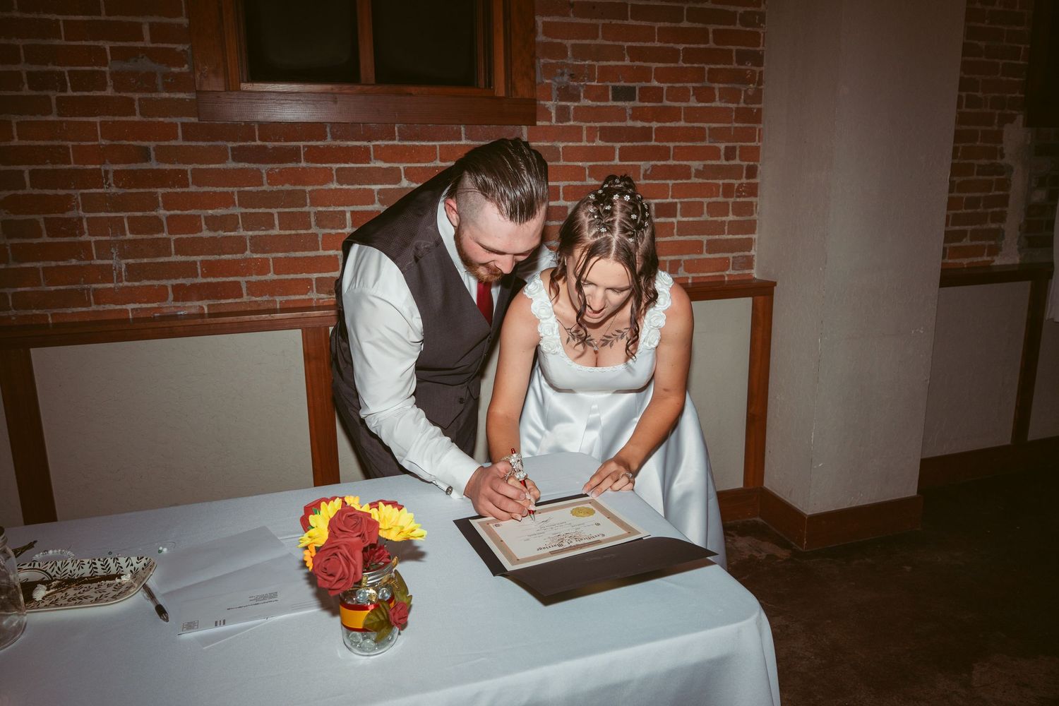 Wedding document signing with bright floral bouquet on table in brick-walled room.