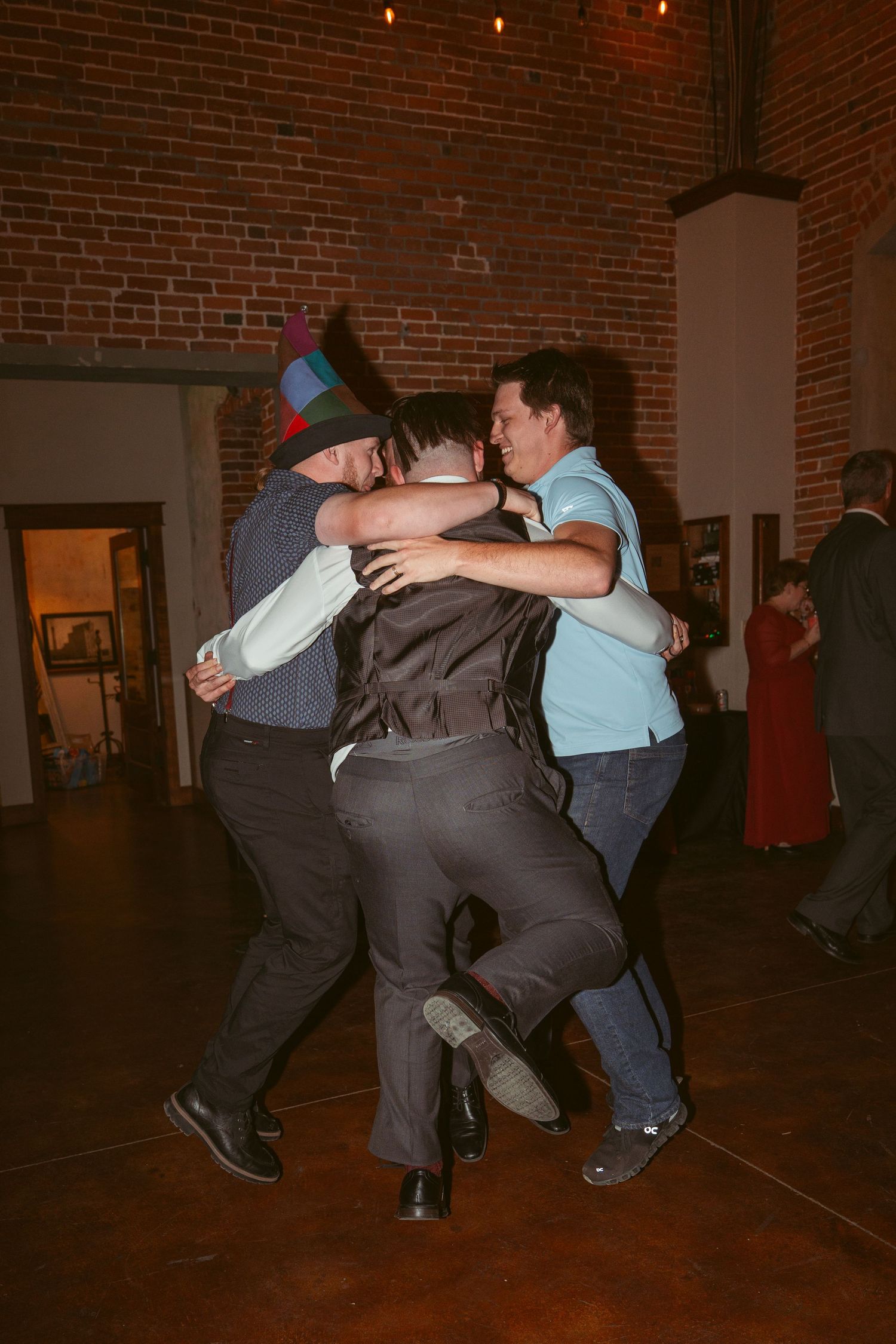 Wedding party members performing synchronized dance moves in a brick-walled reception space.