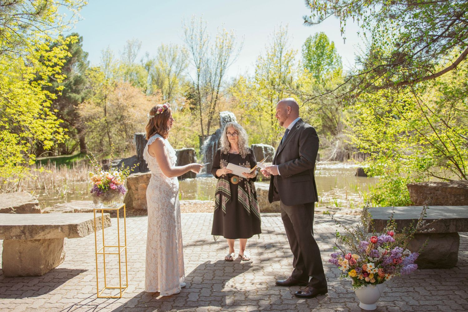 Outdoor wedding ceremony takes place in a scenic garden setting with autumn trees and natural light.
