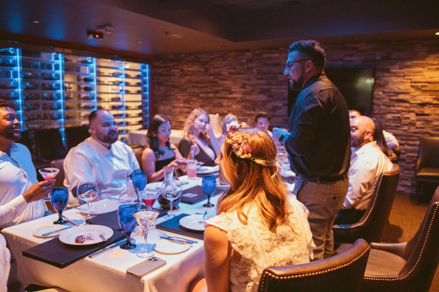 Reception dinner setting with blue ambient lighting and stone wall backdrop.