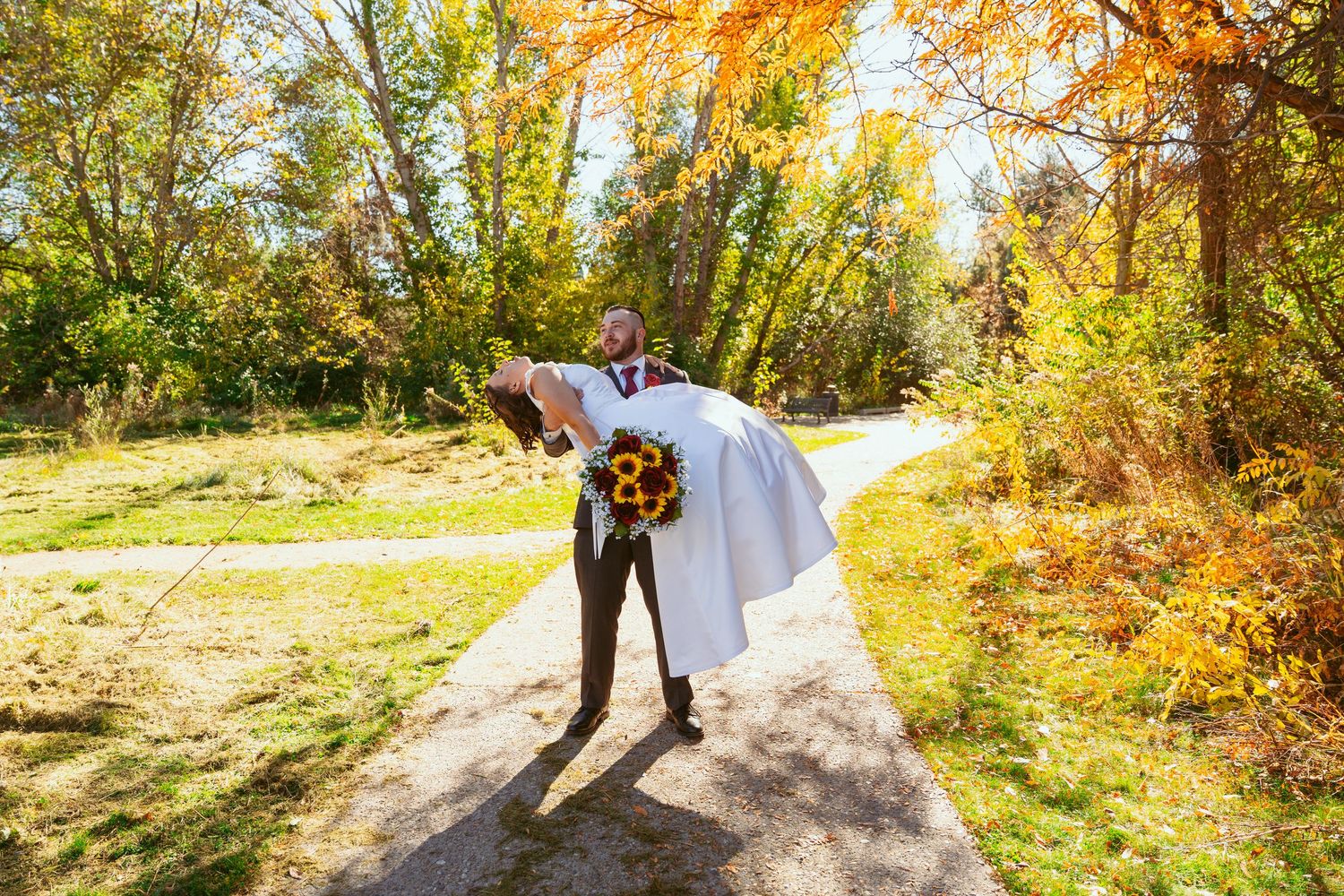 Wedding couple dancing in a scenic autumn setting with golden leaves.