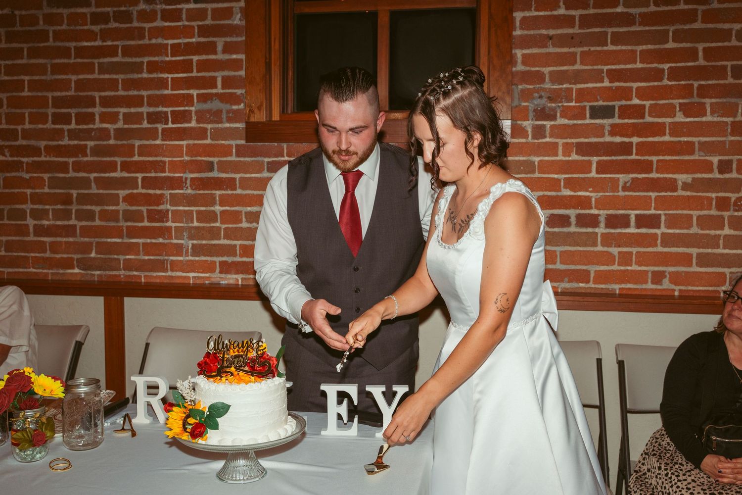 Wedding reception cake cutting moment with couple in front of exposed brick wall.