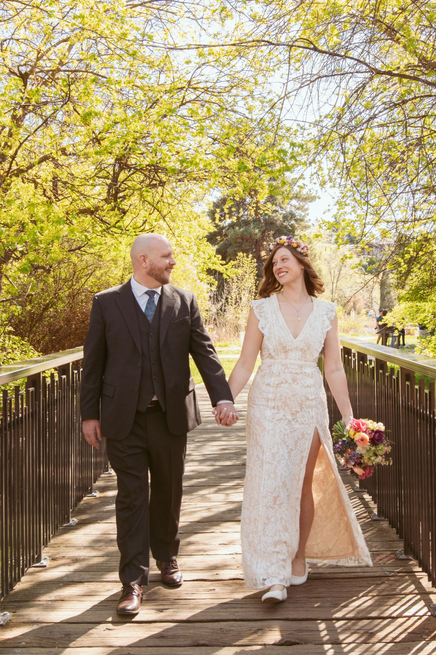 Couple walks hand in hand along wooden bridge pathway surrounded by autumn foliage.