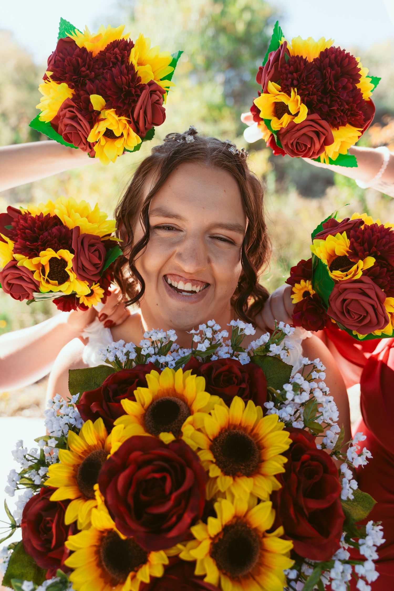 Vibrant floral crown with burgundy roses and yellow sunflowers against natural outdoor backdrop.