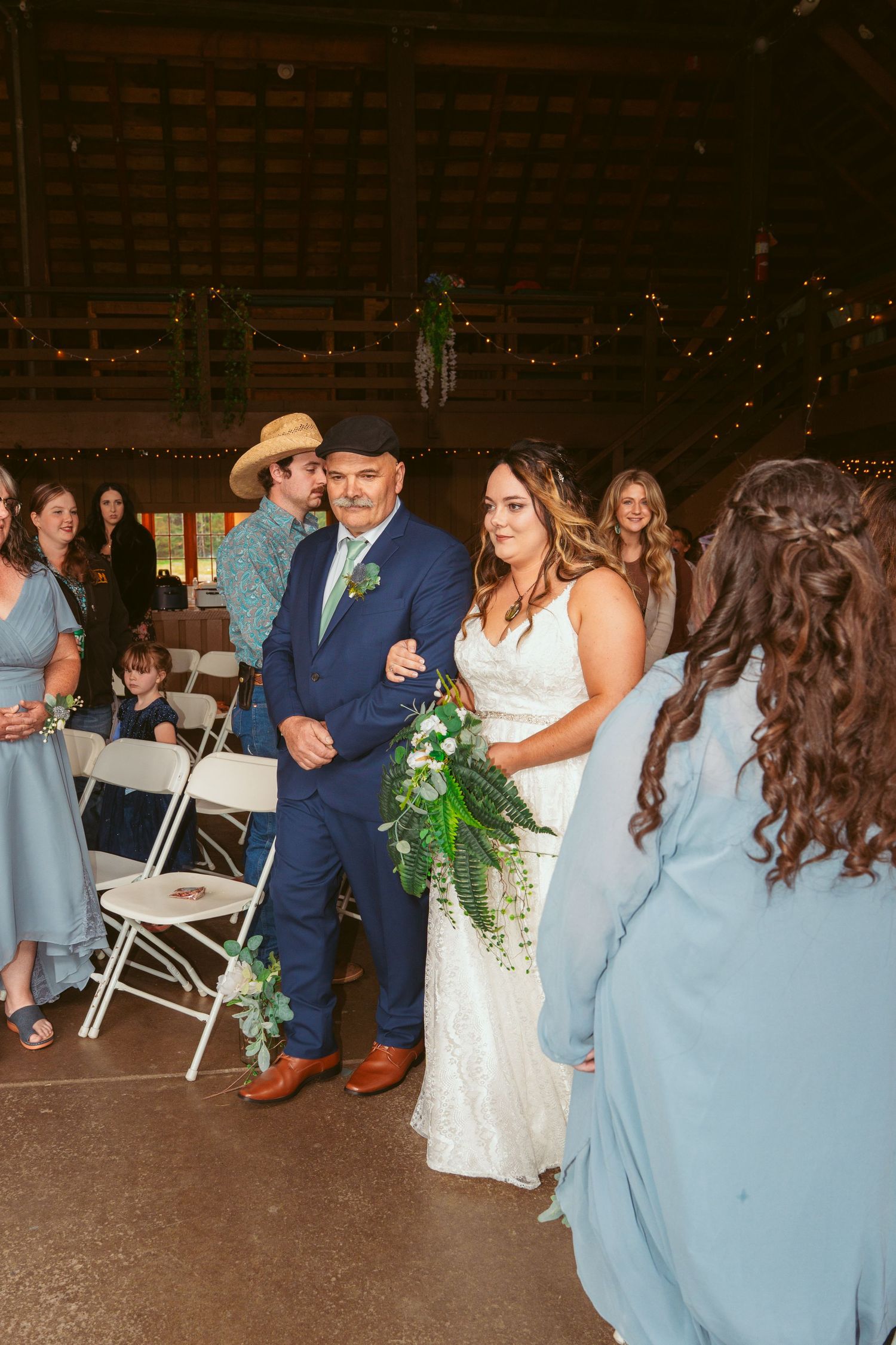 Wedding celebration inside barn with bridesmaids in light blue dresses and groomsmen in navy suits.