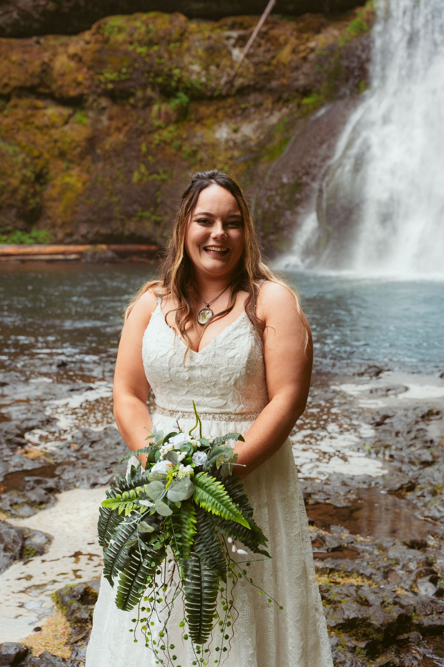Beautiful wedding portrait featuring a lace dress and cascading bouquet against a scenic waterfall backdrop.