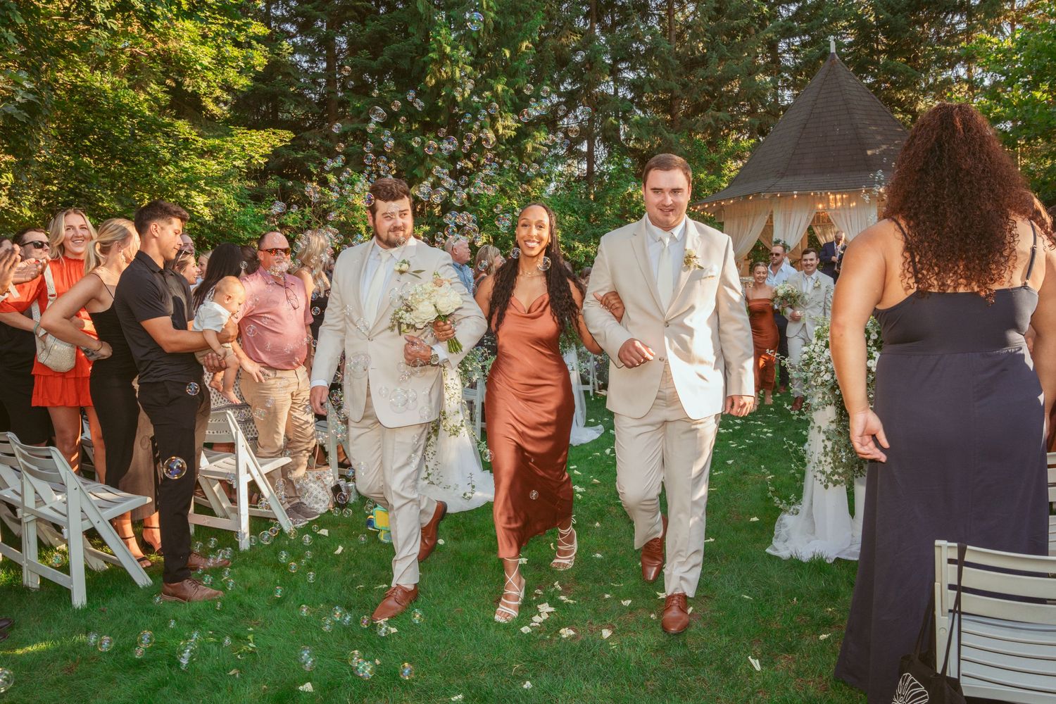 Wedding party processional on grass with attendants wearing coral and cream colored outfits.