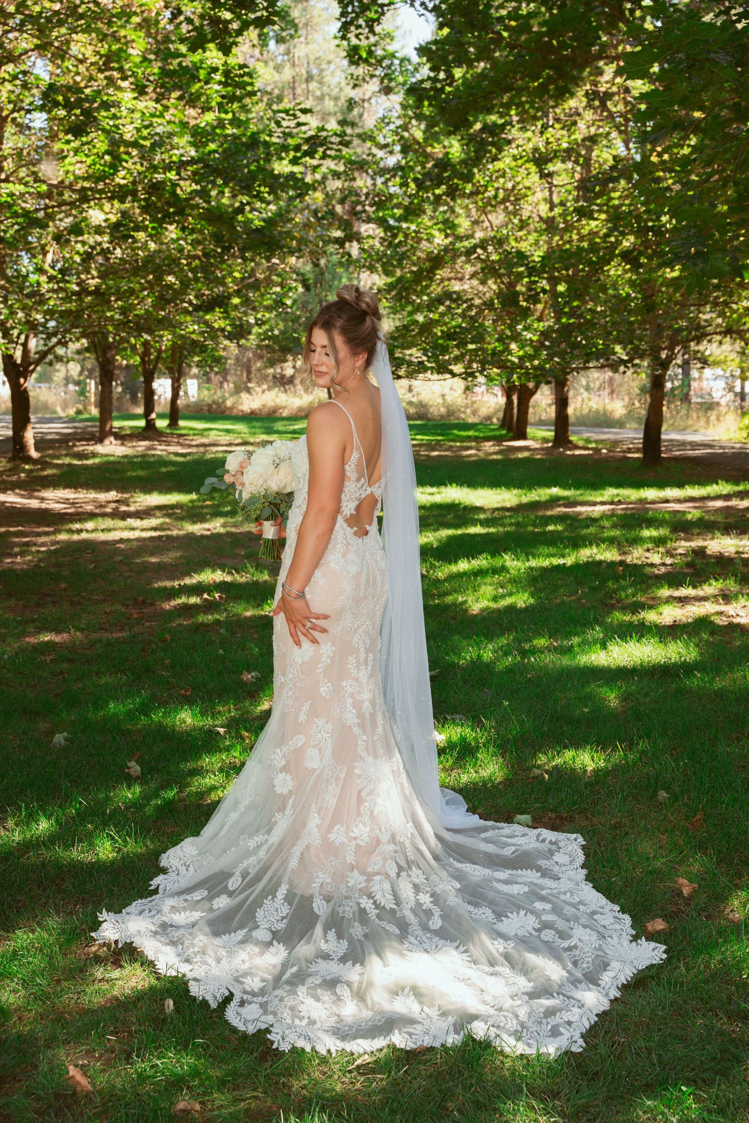 Elegant lace wedding dress with flowing train photographed in a sunlit garden setting.