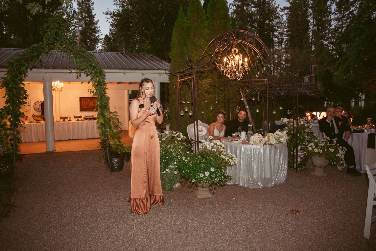 An outdoor evening wedding reception with elegant chandelier lighting and floral decorations.