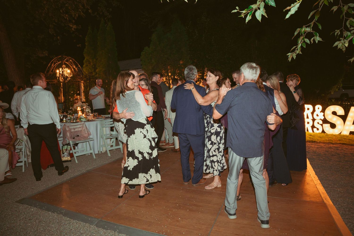 People dancing and celebrating at an outdoor evening party under string lights.