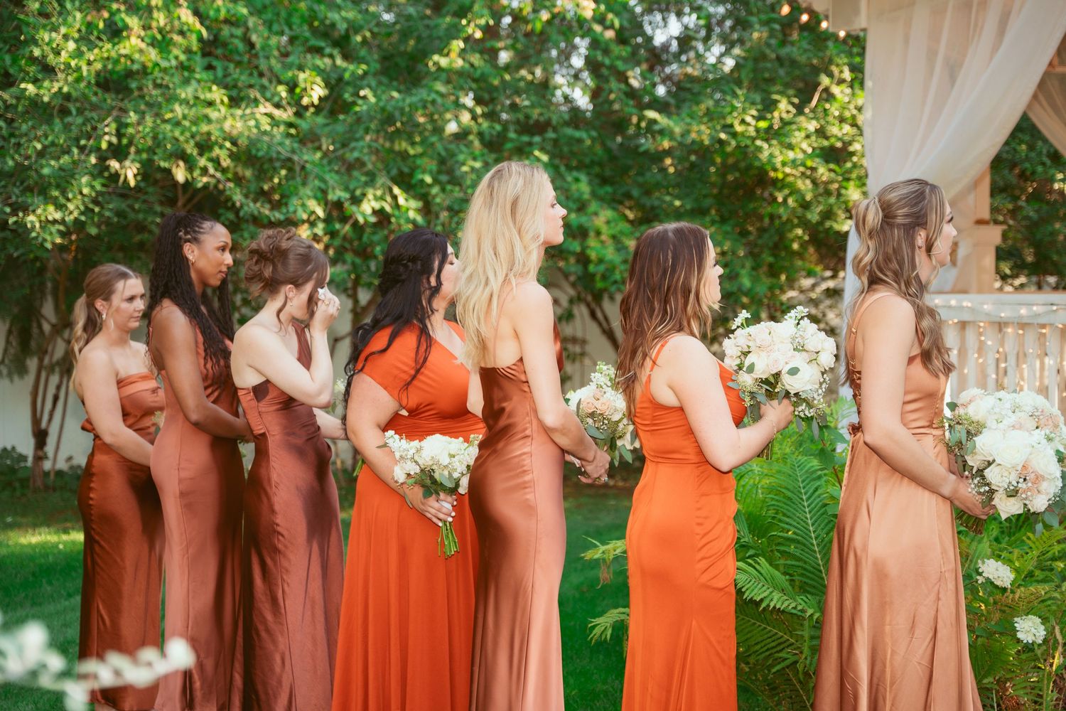 Wedding party in coral and peach dresses standing together in garden setting.