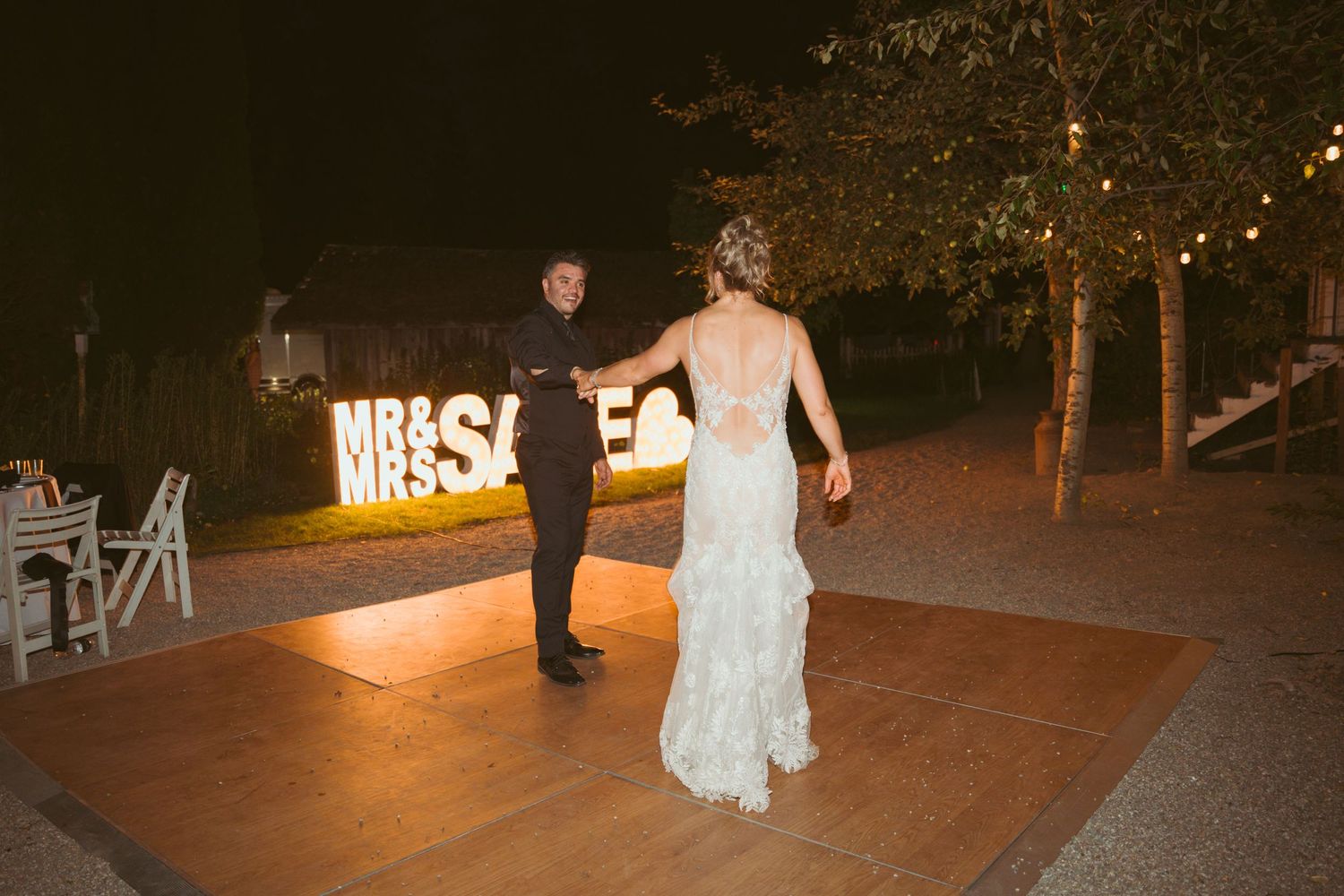 Illuminated outdoor wedding venue at night with glowing signage and string lights.