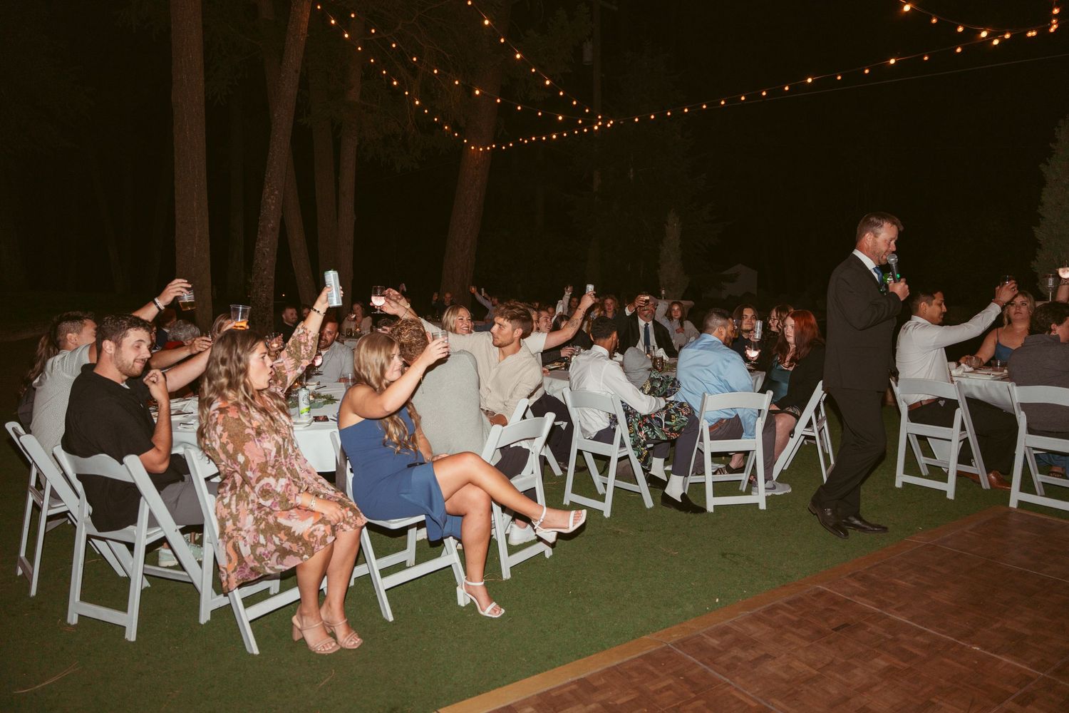 Wedding reception venue at night with string lights and white chairs arranged in rows.