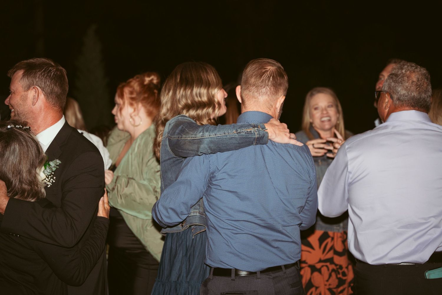 Wedding guests dance together at a nighttime outdoor reception.