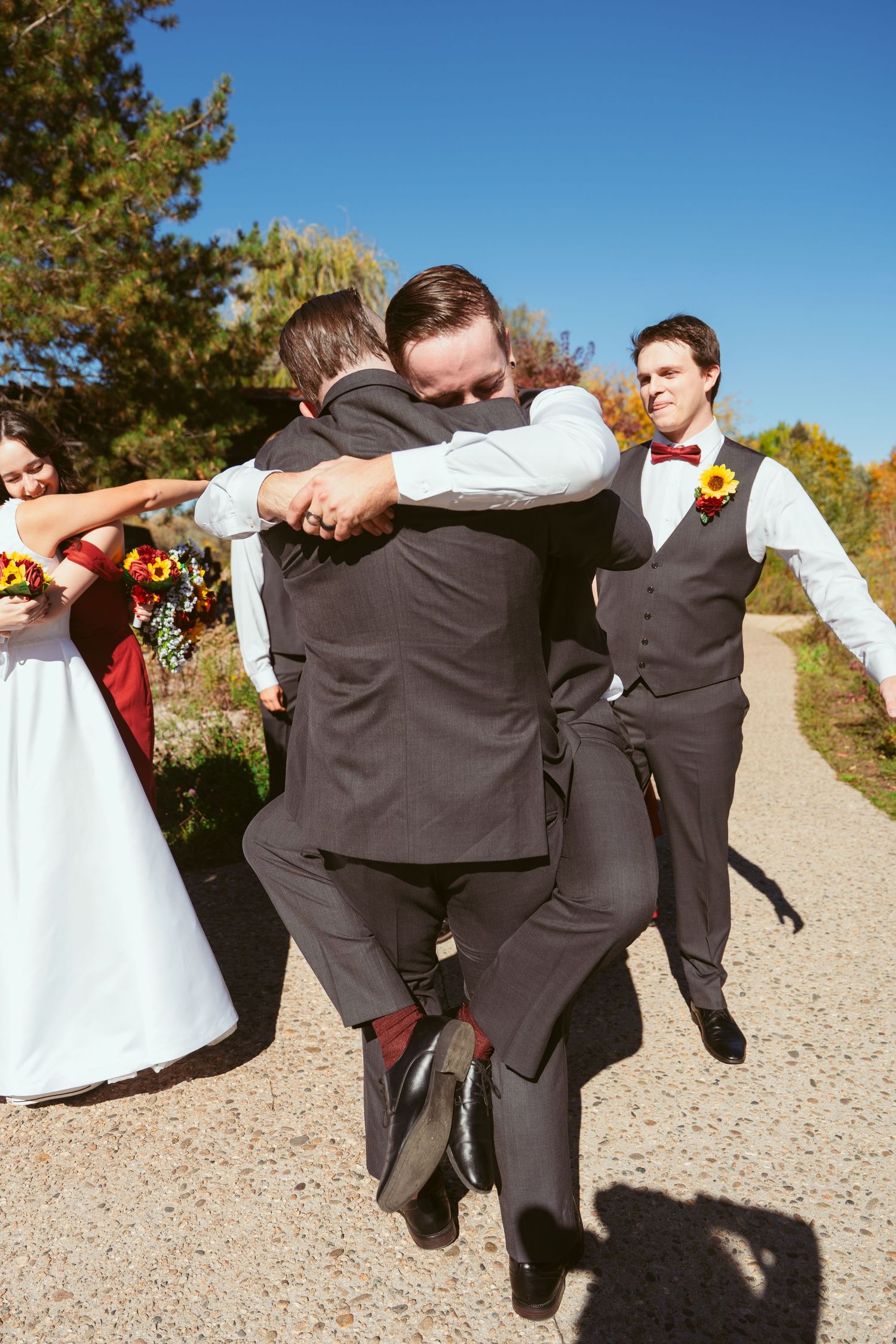 Groomsmen performing playful jumping poses on a gravel path during wedding photos.