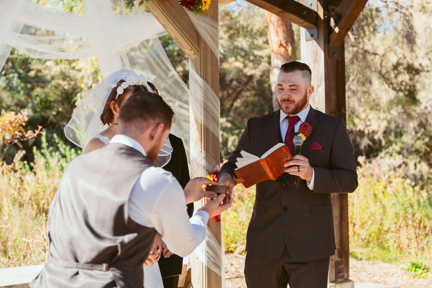 Wedding ceremony participants reading from booklets under a decorated outdoor pavilion.