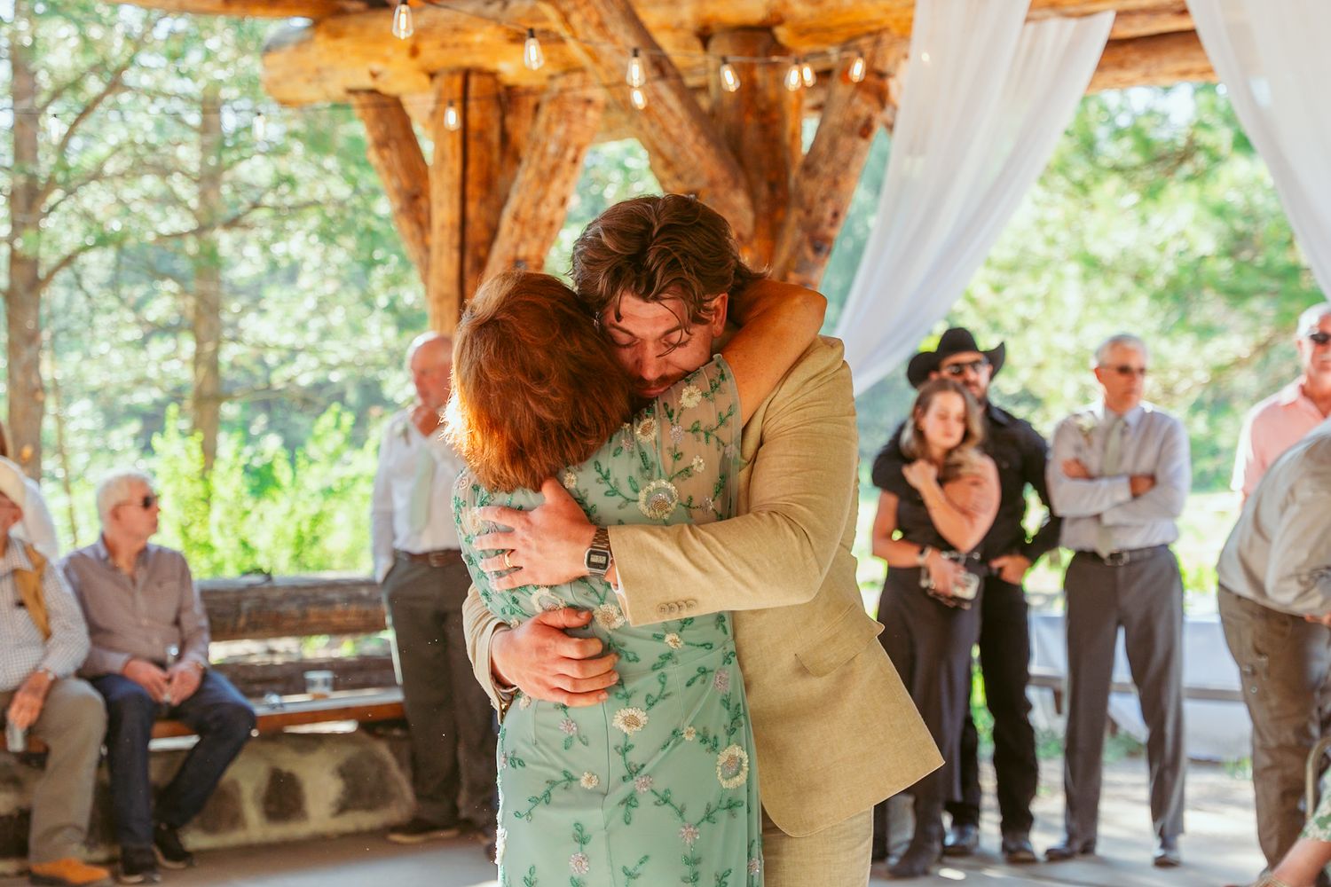 Wedding party dances together during a joyful celebration in a rustic outdoor pavilion.