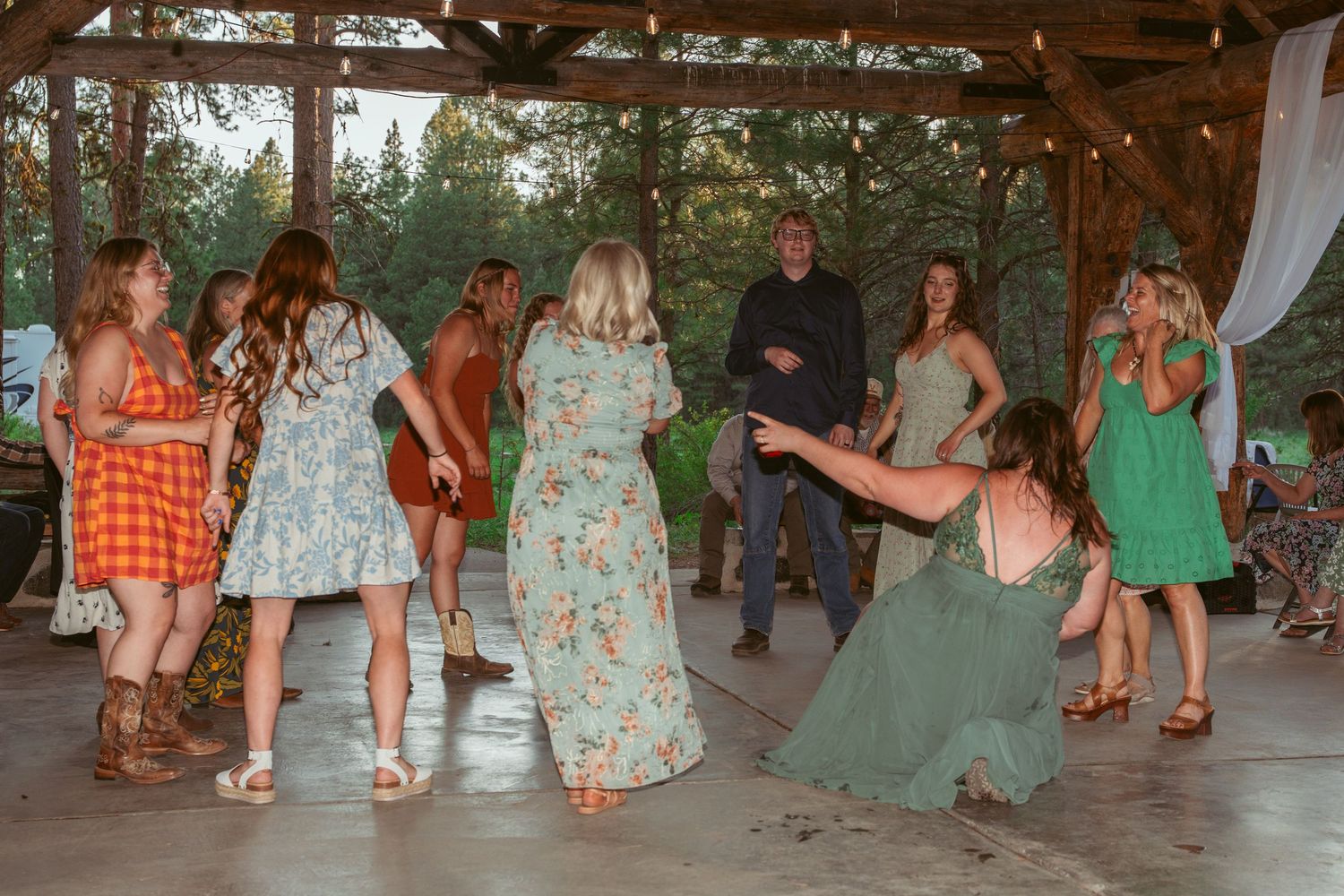 People dancing and celebrating at an outdoor reception under timber beams.
