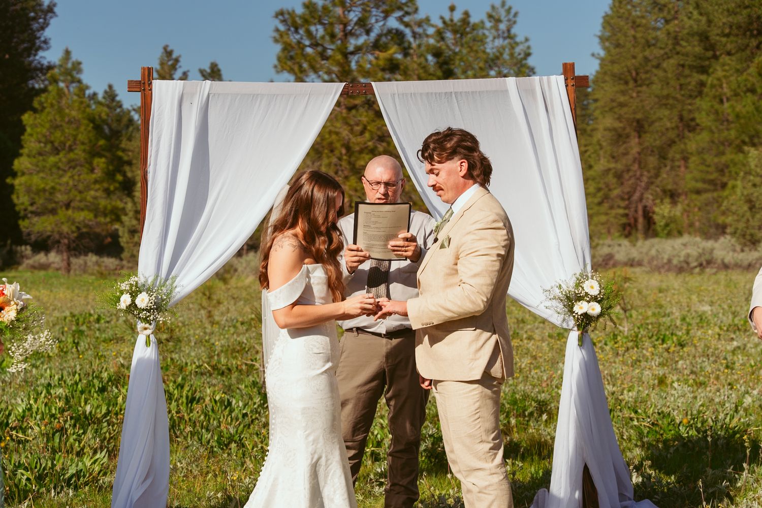 Wedding ceremony unfolds under elegant white drapery with mountain forest scenery.
