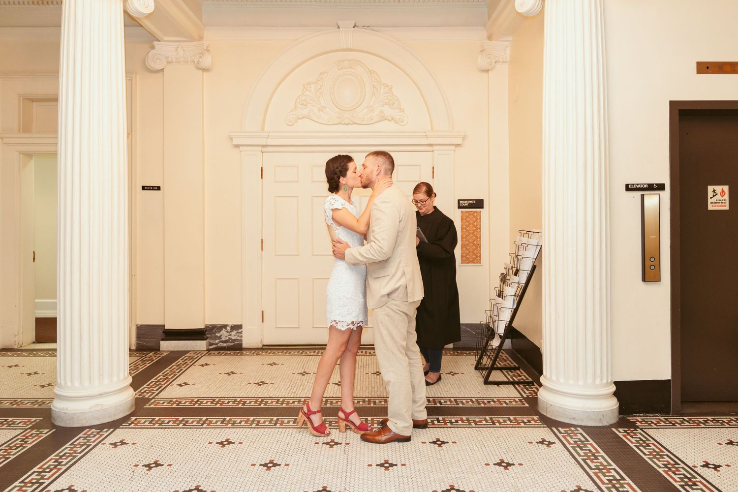 Wedding couple dancing in an elegant room with white columns and checkered floor.