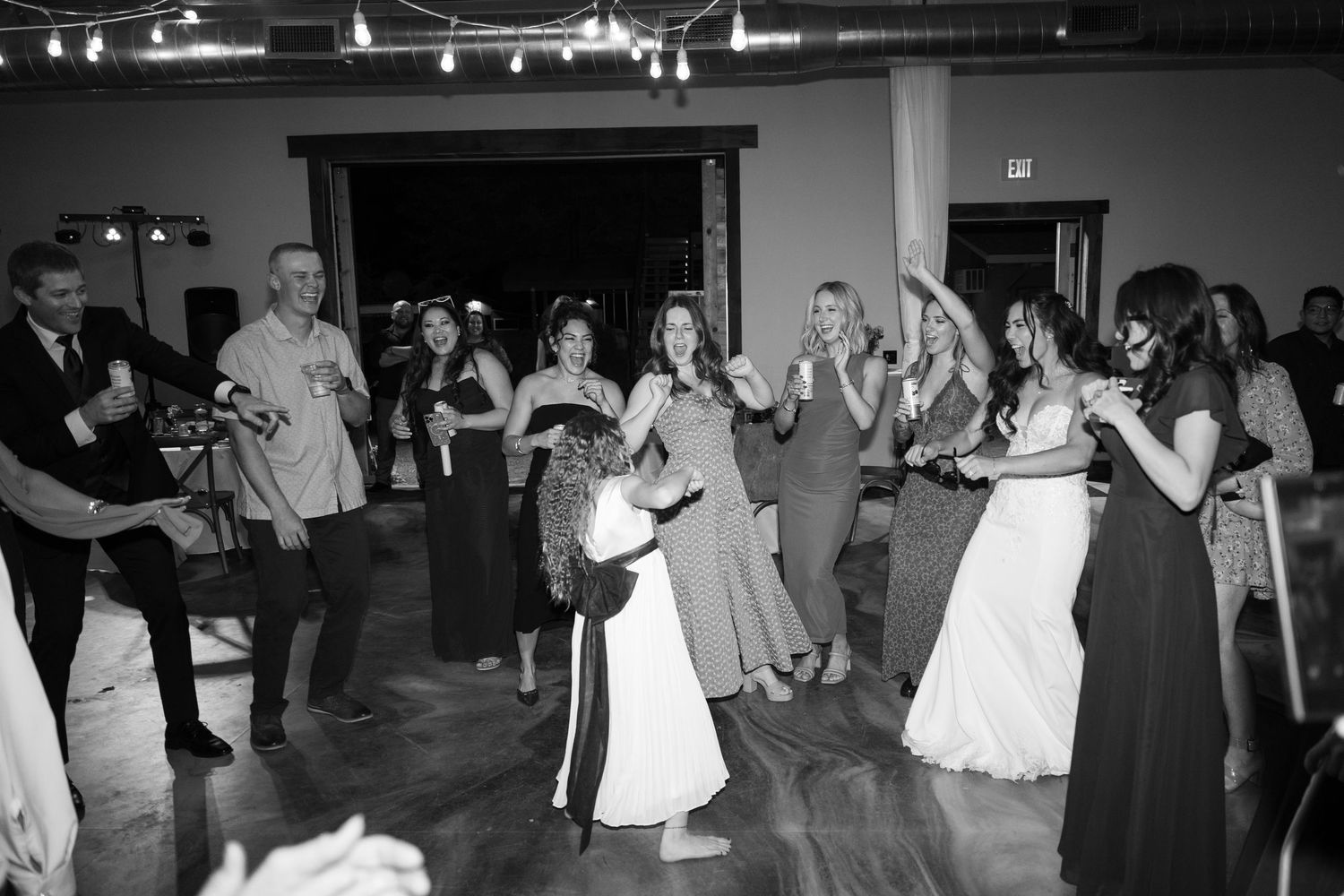 Black and white photo of wedding guests dancing and celebrating in a reception venue.