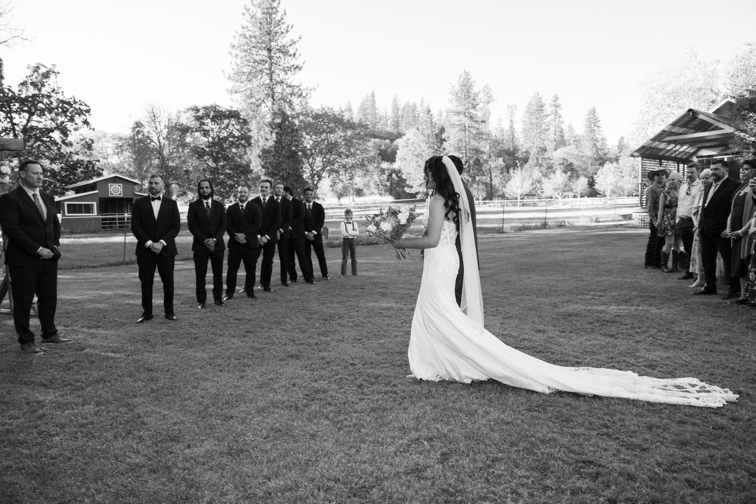 Black and white wedding ceremony processional with guests lined up on lawn.