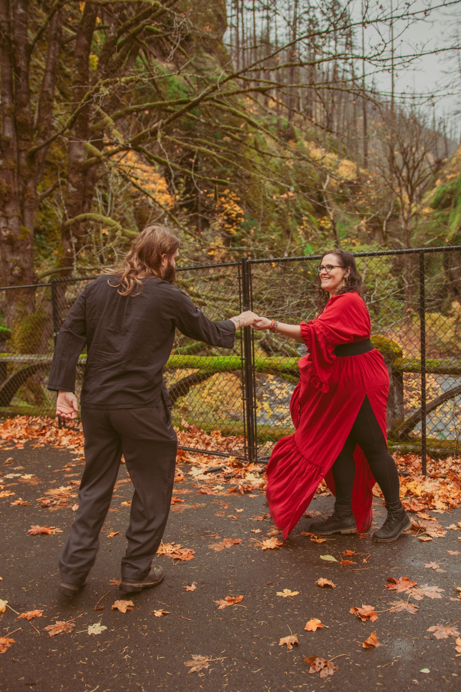 A couple performing dance lifts and spins on a path surrounded by autumn trees.