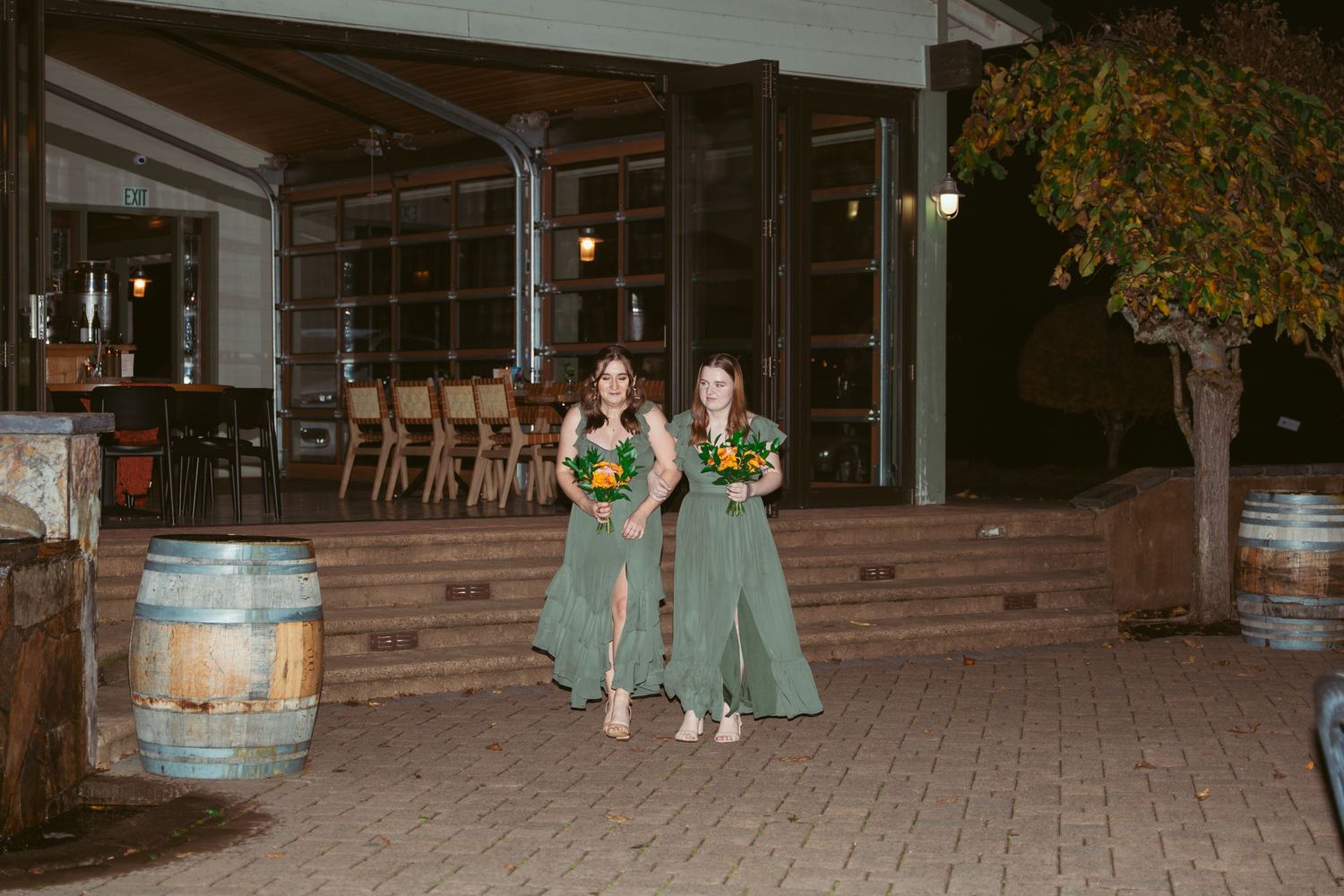 Wedding party members in light gray suits gather outside a venue at night.