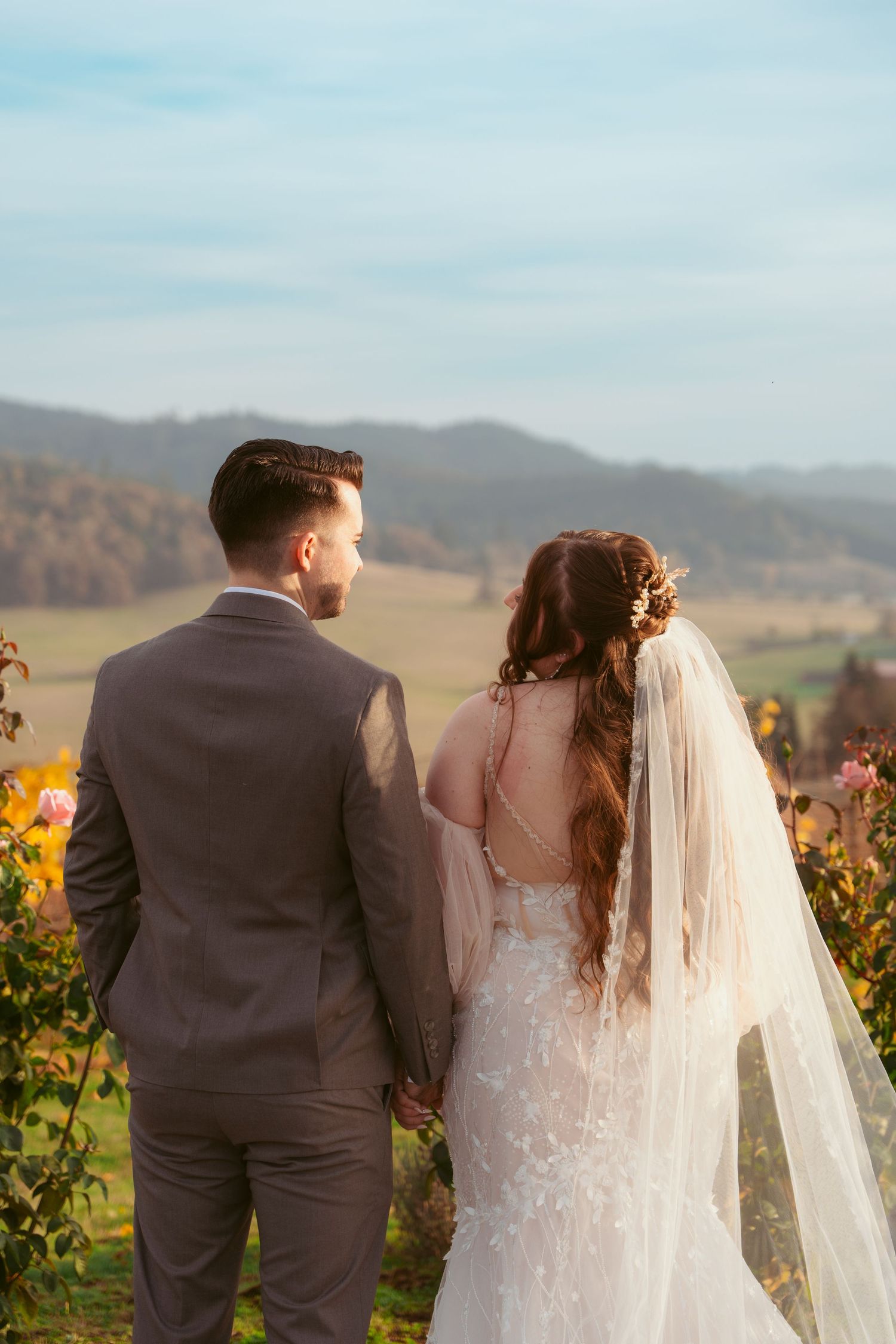 Couple shares tender moment among vineyard rows with mountain landscape behind them.