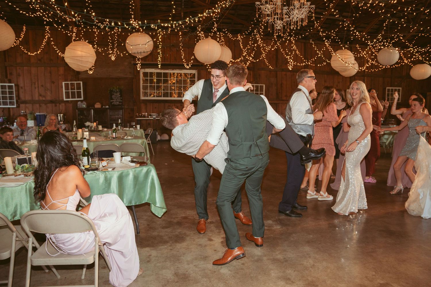 Couples dancing at a wedding reception under glowing string lights and white paper lanterns.