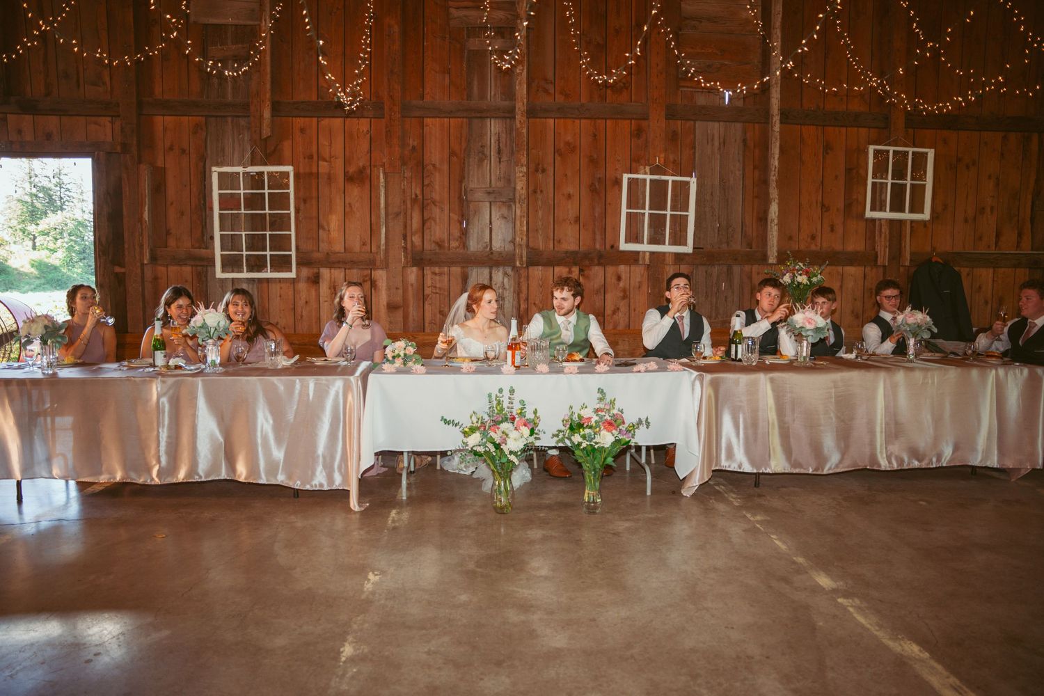 Wide angle shot of barn wedding reception with string lights and elegant table settings.