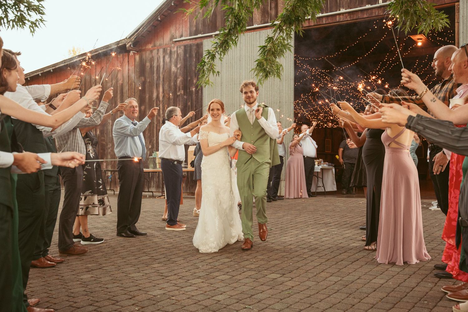 Wedding celebration with sparkler sendoff as couple walks between rows of guests at sunset.