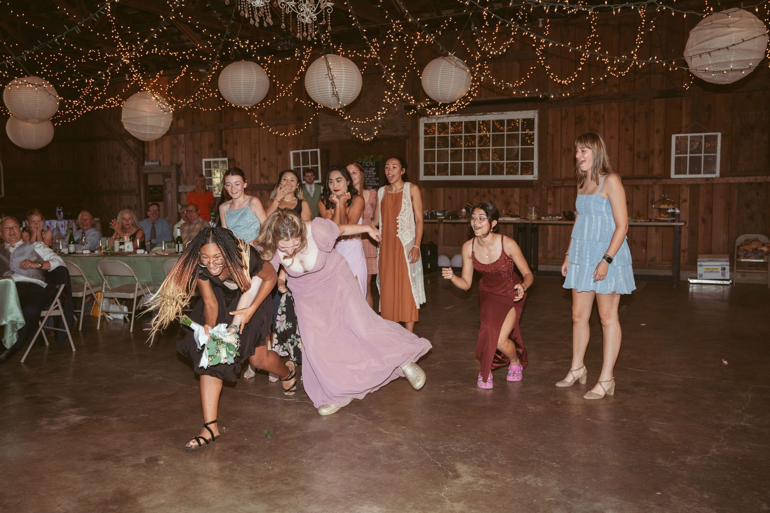 Guests dancing and celebrating at a barn wedding reception under warm lighting and paper lanterns.