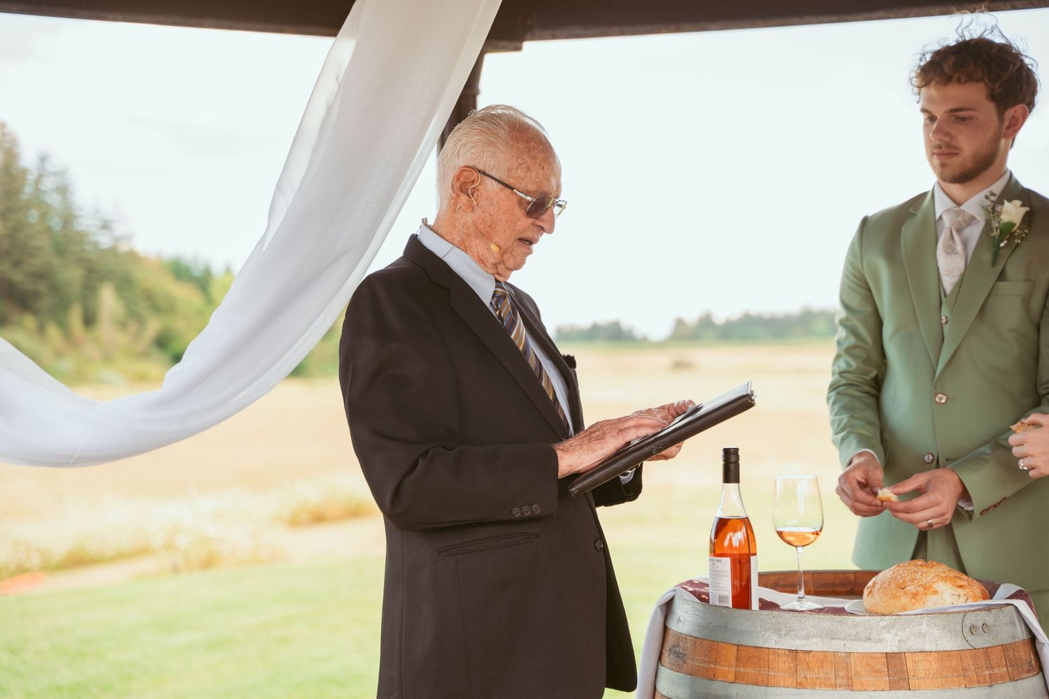 Wedding ceremony participants sharing documents under wooden gazebo.