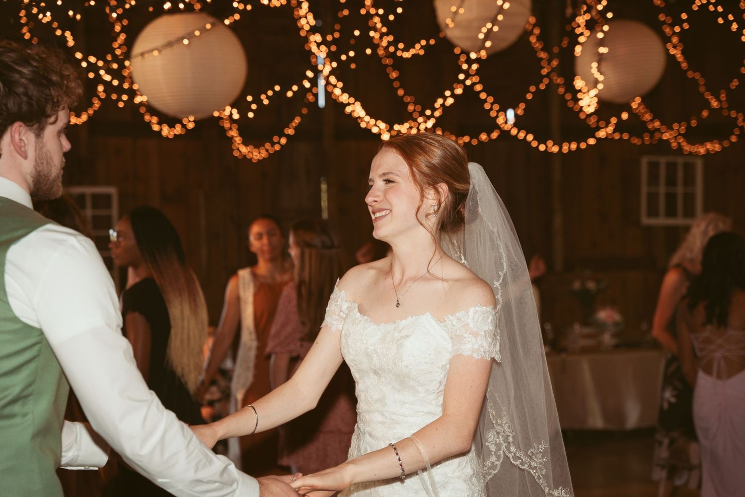 Couple sharing their first dance at a wedding reception under glowing string lights and lanterns.