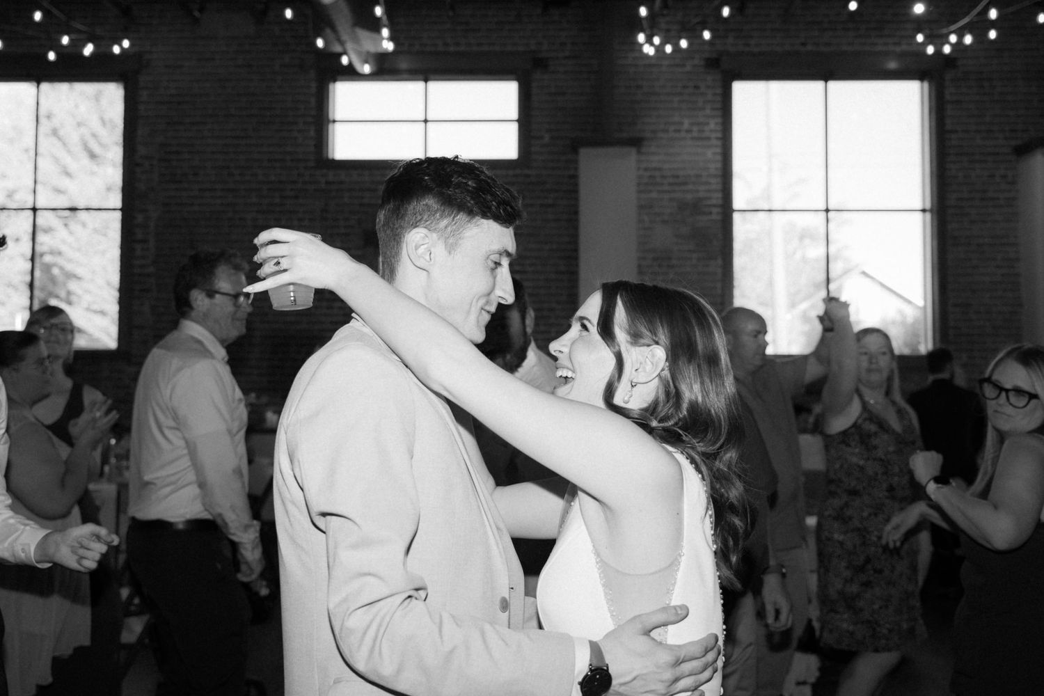 Wedding reception dance party in a dimly lit brick venue with twinkling lights.