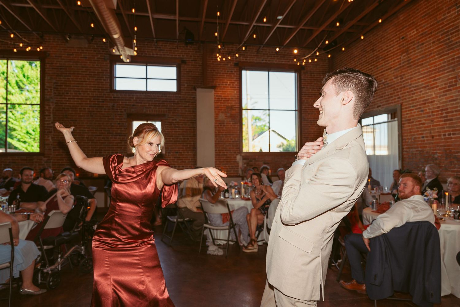 Wedding guests dance beneath twinkling lights in a converted brick building venue.