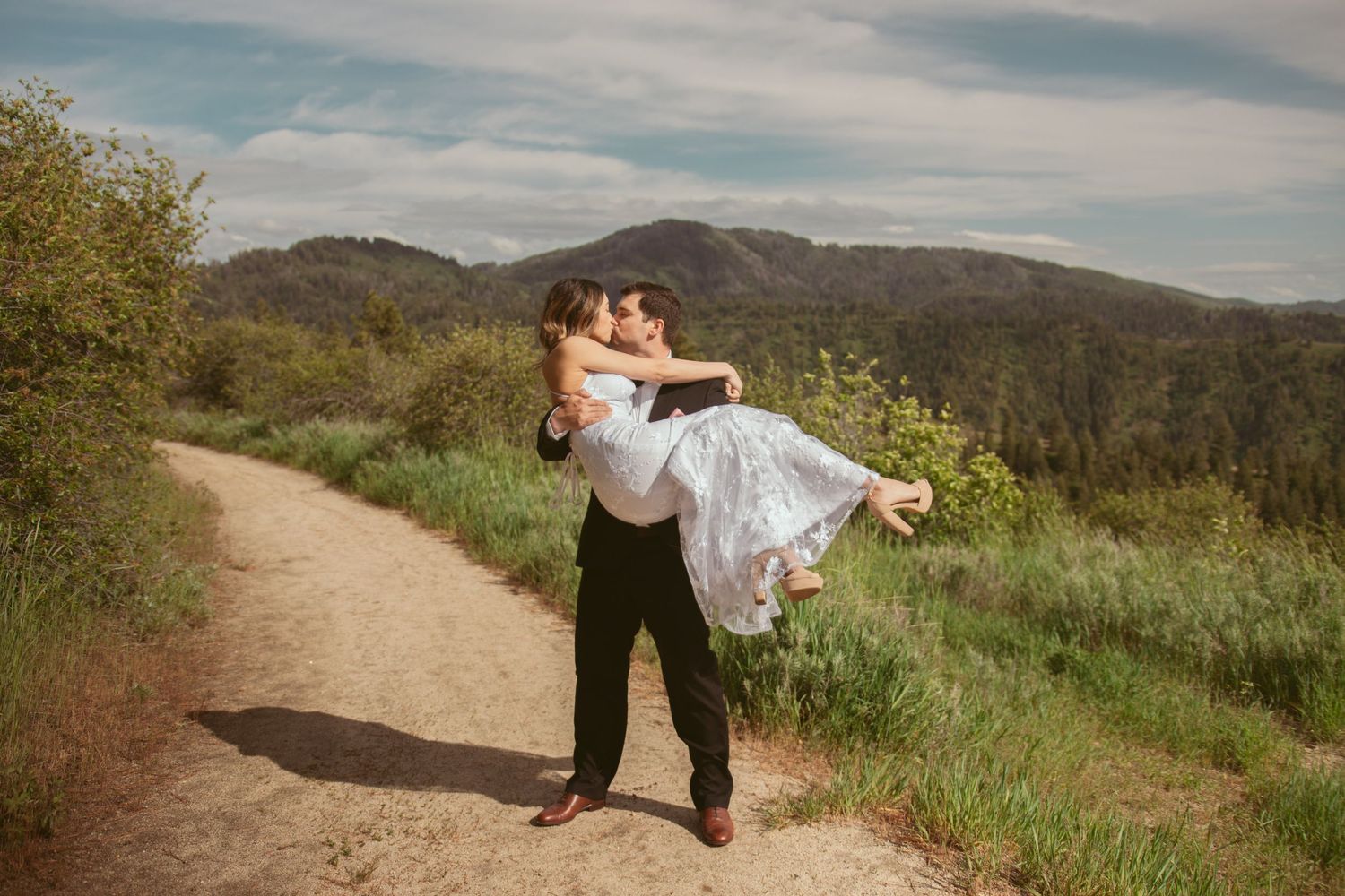 A romantic dance dip pose captured on a mountain trail with scenic views in the background.