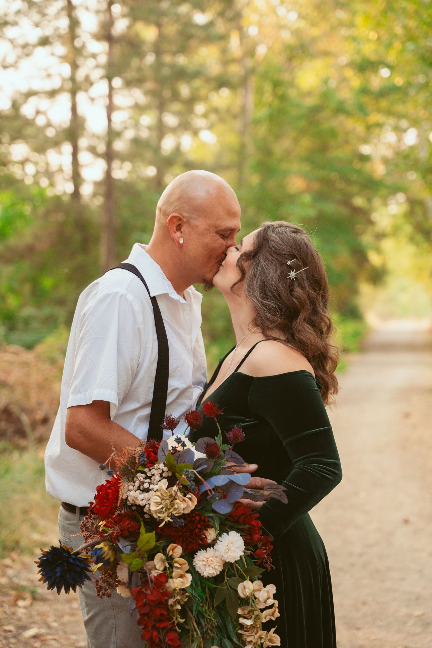 A couple shares an intimate moment outdoors with a stunning fall-colored bouquet featuring deep red flowers.