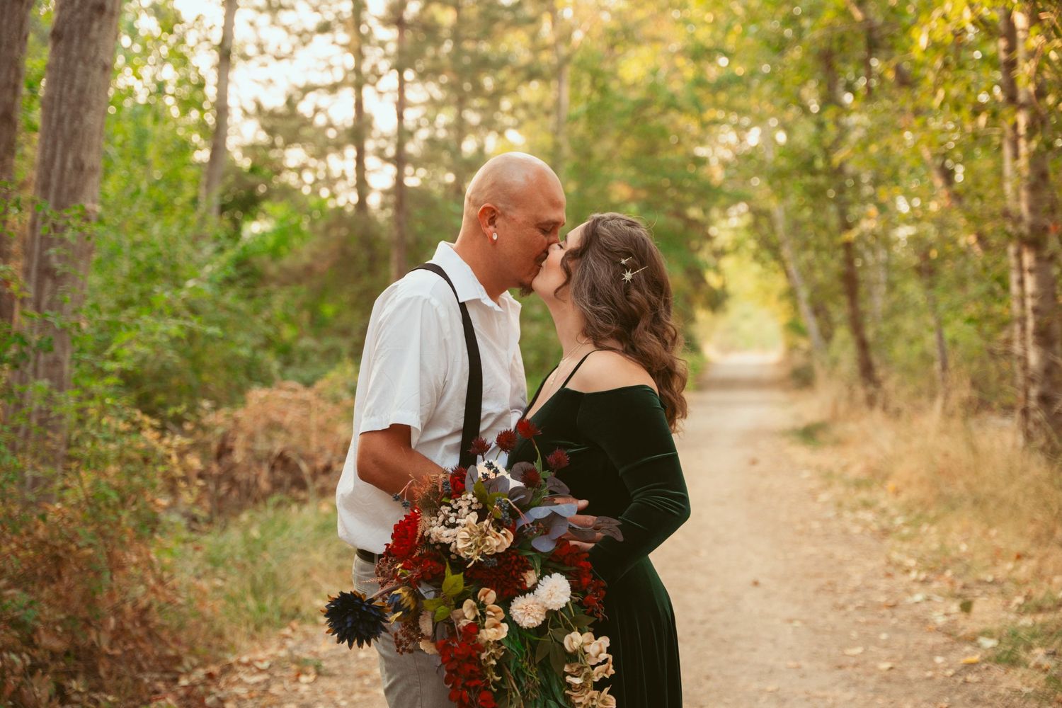 Couple embracing on a sunlit forest path with autumn colors in background.