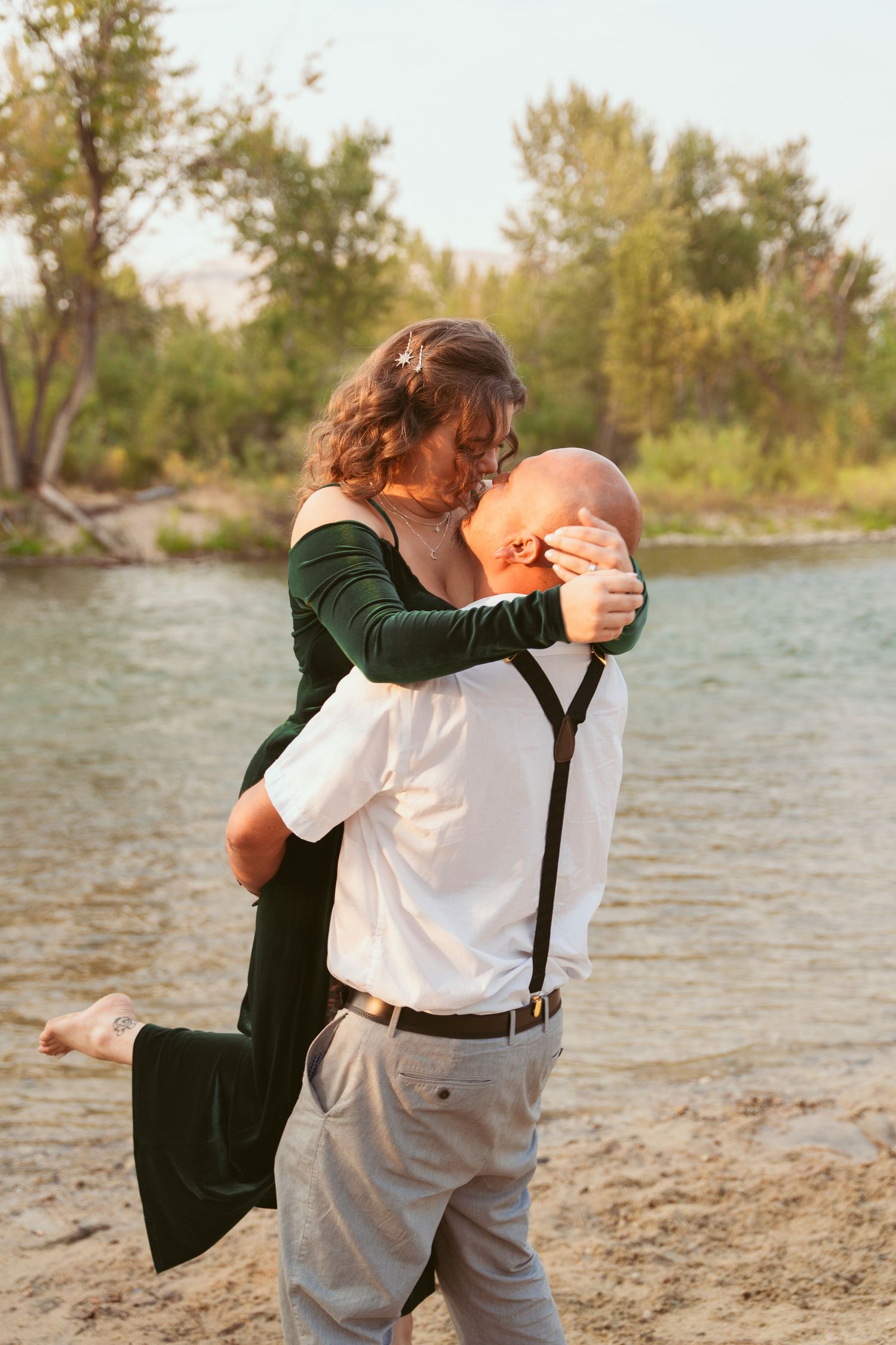 A couple dances playfully on a beach near the water.