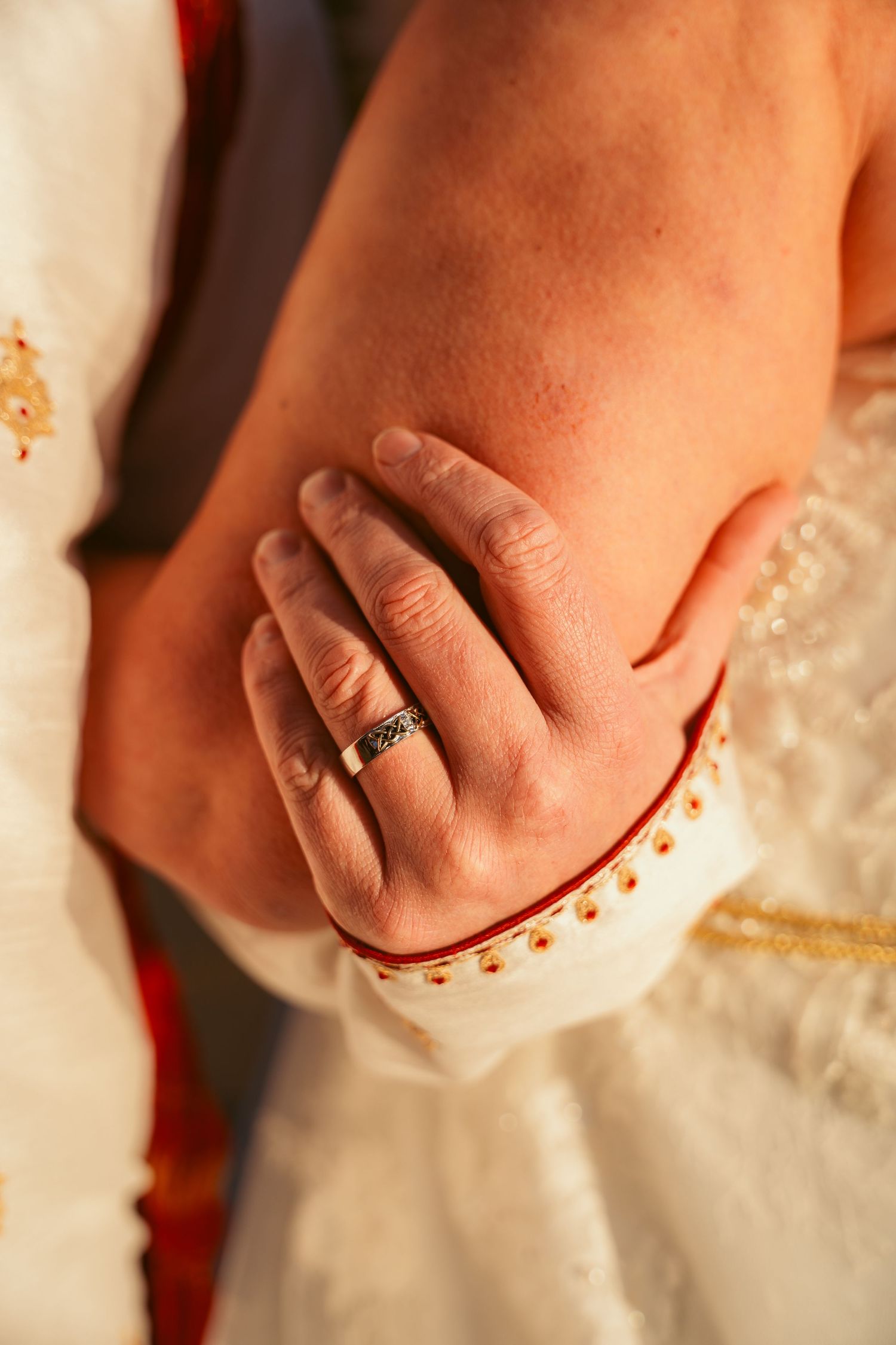 Close-up of hands with wedding rings against white lace dress fabric.