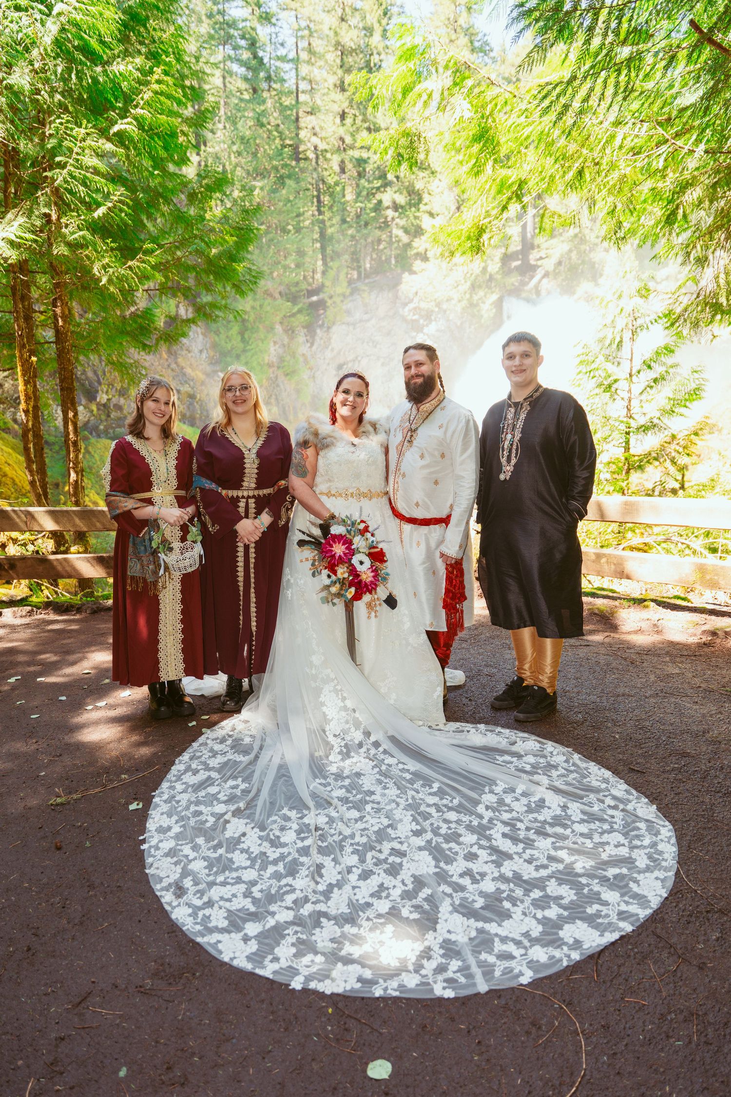 Wedding group photo showcasing a stunning white dress with an elaborate train on forest ground.