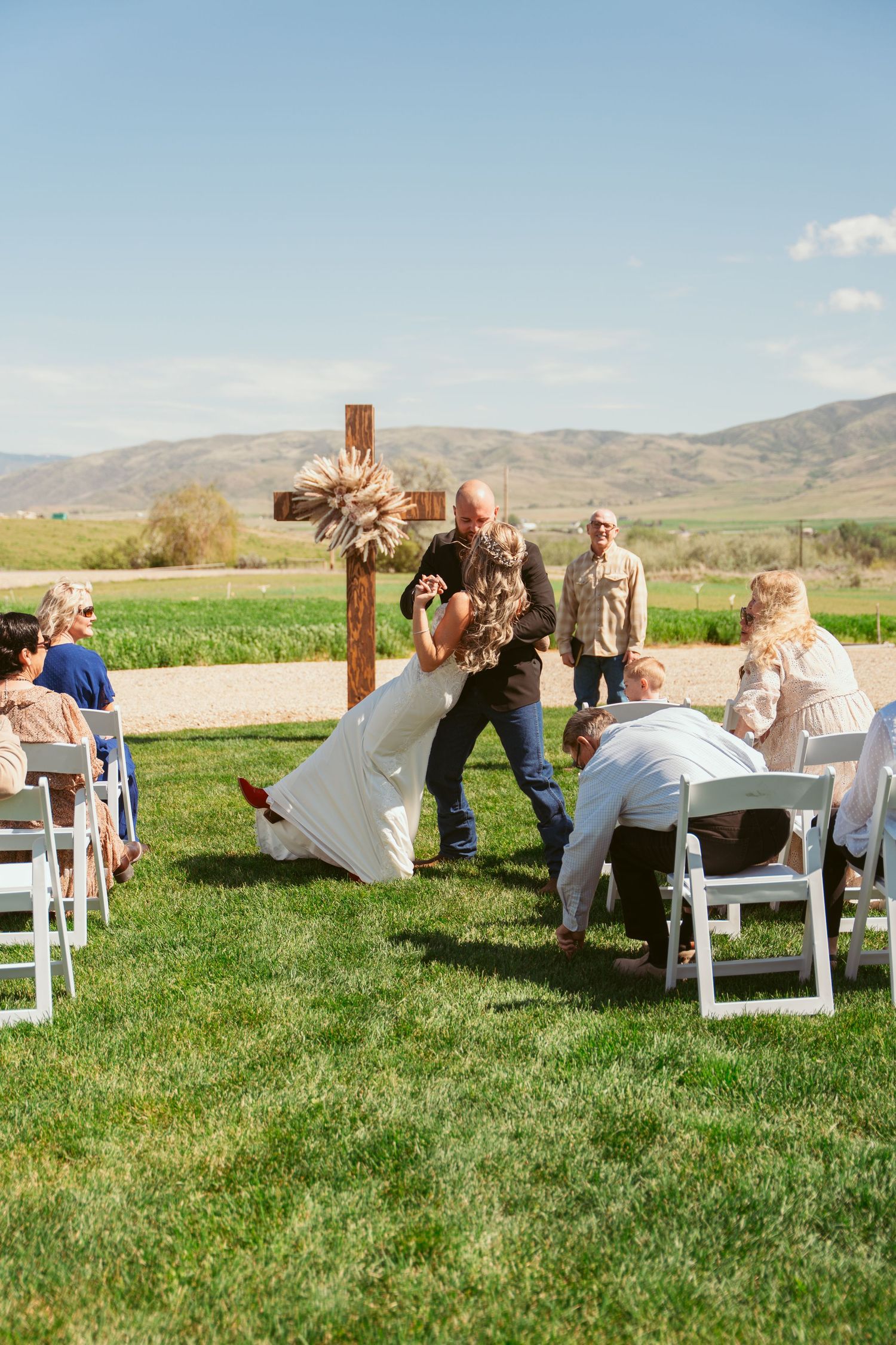 A joyful moment during an outdoor wedding ceremony with guests looking on from white chairs.