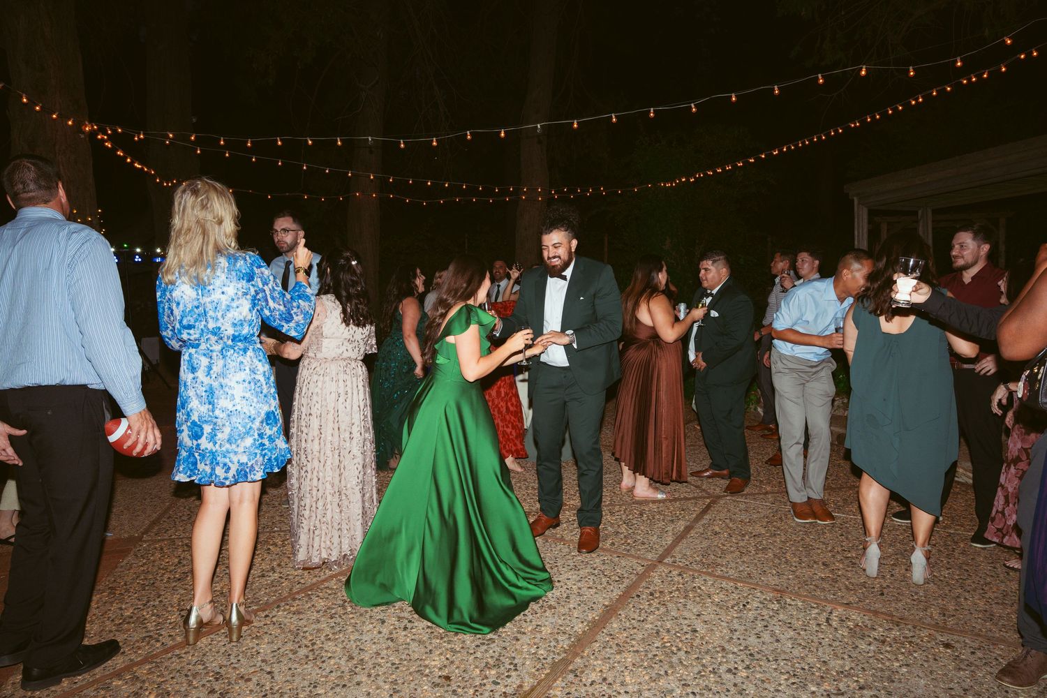 Nighttime wedding celebration with guests dancing under twinkling lights.