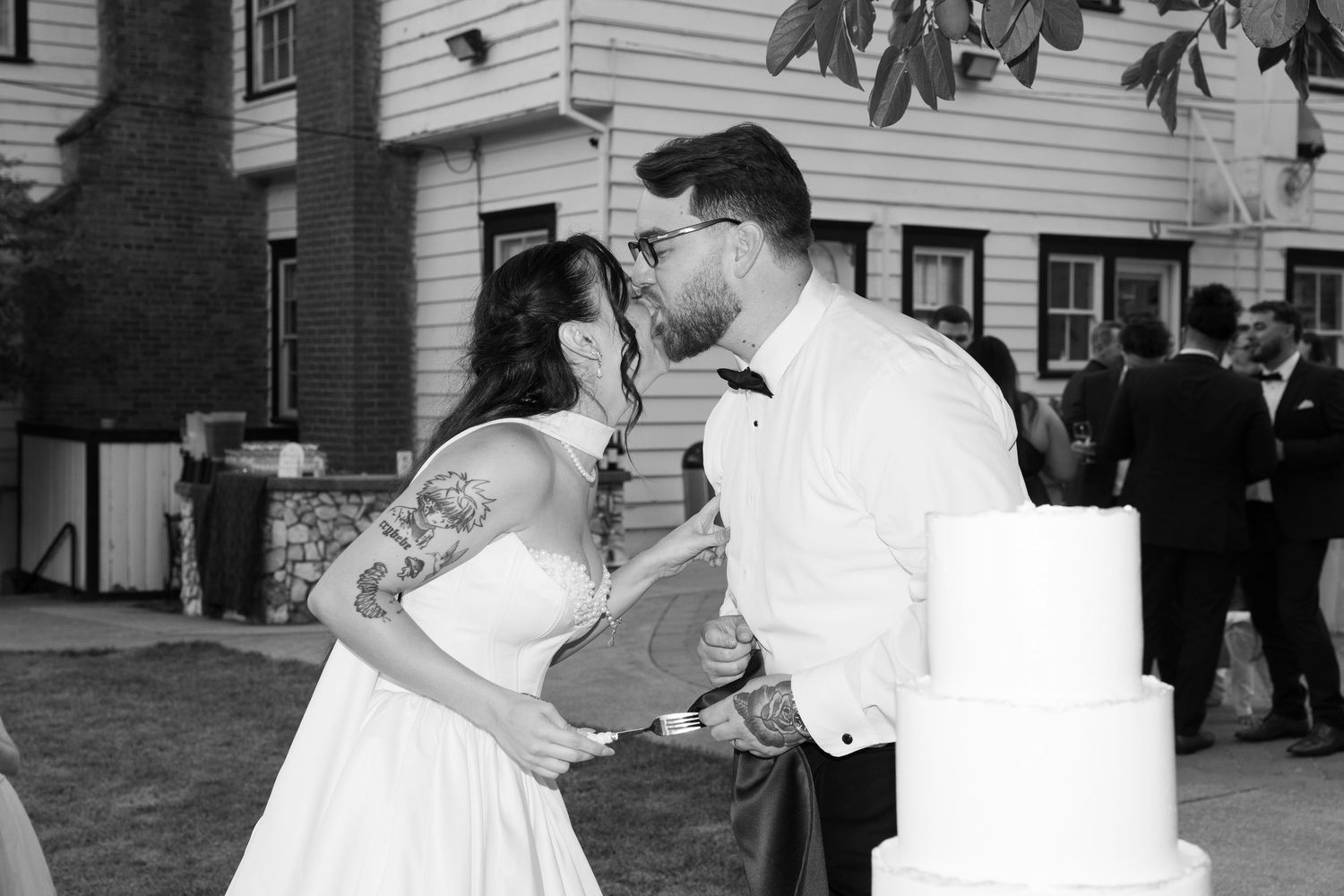 A black and white photo captures a playful cake-feeding moment at a wedding.